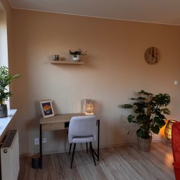 Pracownia Psychoterapii AGATA NIEDŹWIEDŹ-DĄBKOWSKA - Neutralne wnętrze gabinetu z biurkiem, krzesłem i roślinami. Ciepłe, beżowe ściany, drewniana podłoga. Przytulna aranżacja sprzyjająca skupieniu i relaksacji.