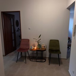 Pracownia Psychoterapii AGATA NIEDŹWIEDŹ-DĄBKOWSKA - Przytulny kącik w poczekalni: dwa krzesła (różowe i zielone) po bokach stolika z rośliną, świecą i radiem, tworzące relaksującą atmosferę.