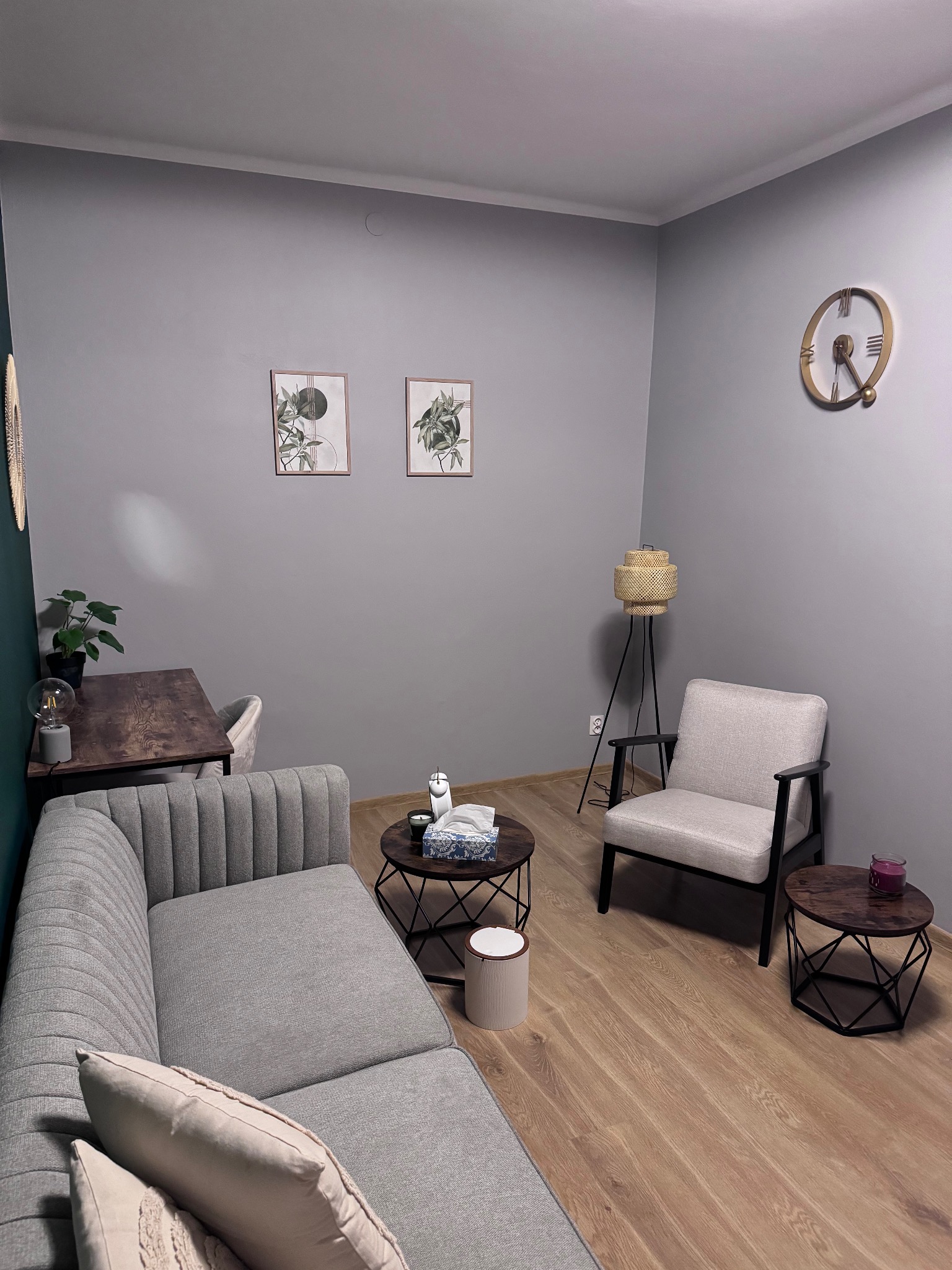 Jasnoszary gabinet z sofą, stolikami kawowymi i lampą podłogową, dekorowany roślinami i obrazkami w ramkach.