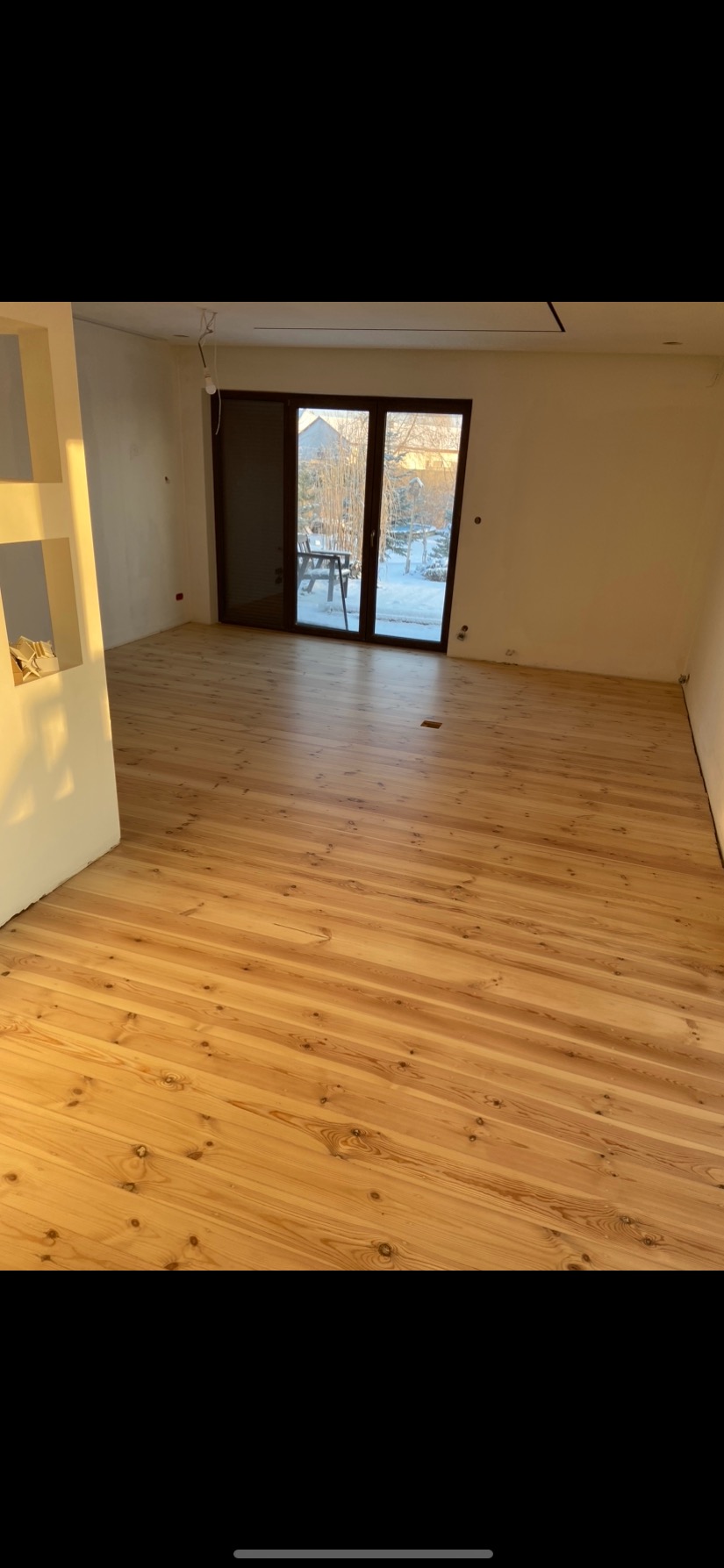Jasne, drewniane deski podłogowe z widocznymi słojami, ułożone w nowym pokoju z dużymi drzwiami balkonowymi i widokiem na zimowy krajobraz.