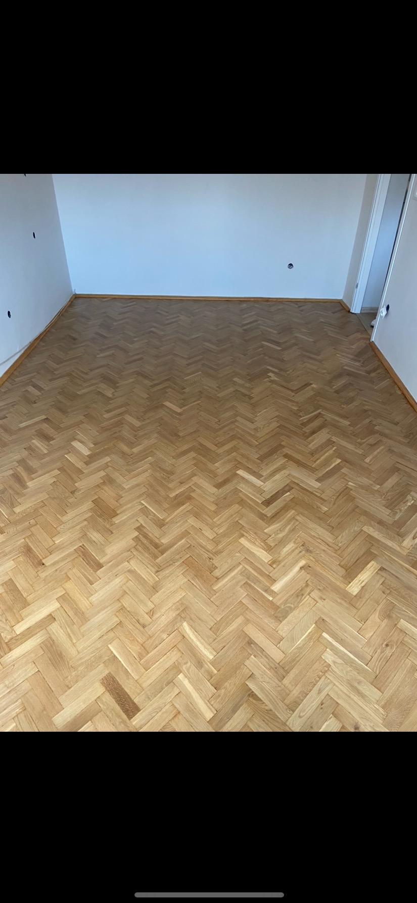 Jasna, nowa podłoga z parkietu ułożonego we wzór jodełki francuskiej, widoczna w pustym pokoju z białymi ścianami i listwami przypodłogowymi.