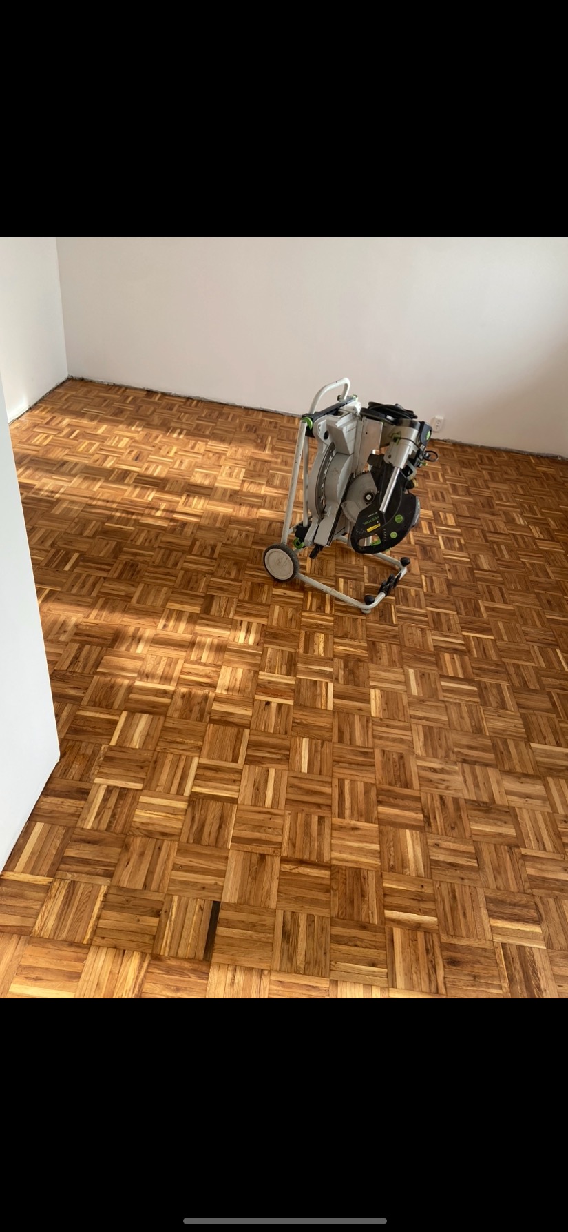 Parkiet w kwadraty, po renowacji, z widoczną szlifierką do podłóg na kółkach.