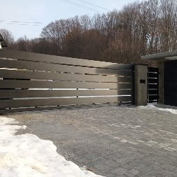 STALVA Piotr Sadkowski - Nowoczesna brama wjazdowa z poziomych, metalowych profili w kolorze szarości, zamontowana na posesji z kostką brukową i resztkami śniegu.