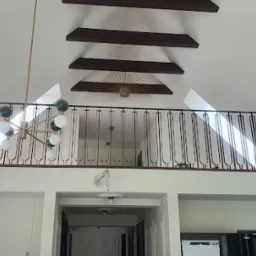 Czarna, metalowa barierka na antresoli w jasnym wnętrzu z drewnianymi belkami stropowymi i nowoczesnym żyrandolem. W tle widoczne okno dachowe wpuszczające światło.