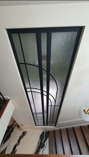 Widok z góry na nowoczesną klatkę schodową z czarną metalową konstrukcją i dekoracyjnym, teksturowanym szkłem, marmurową posadzką i drewnianymi schodami.