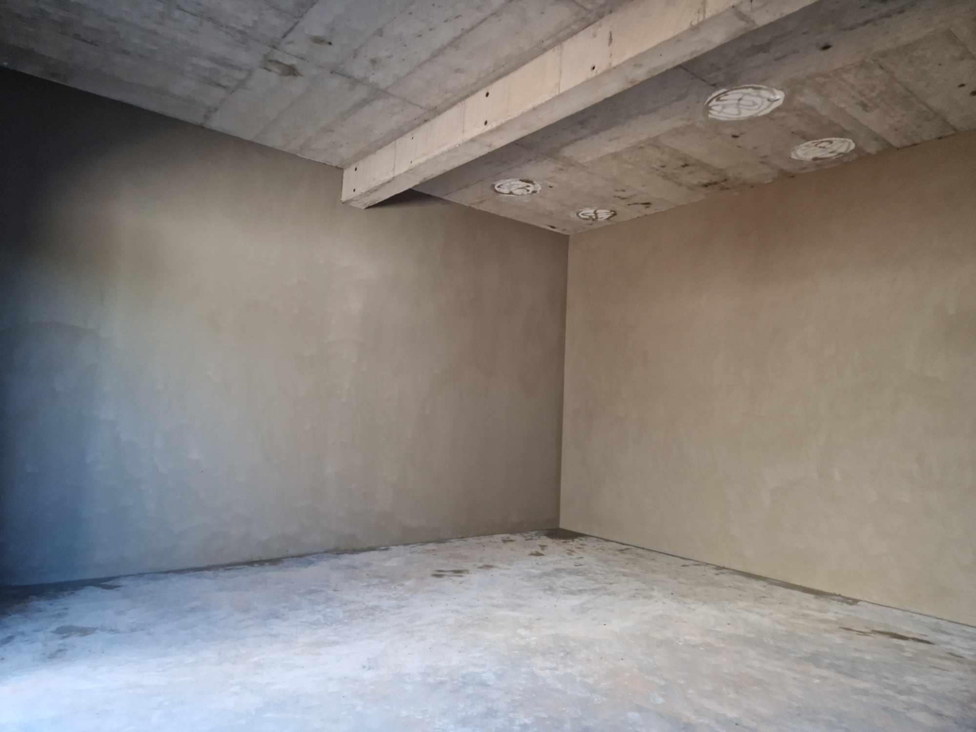 Surowe wnętrze po nałożeniu tynku, widoczne ślady po łatach na suficie pod otwory oświetleniowe.