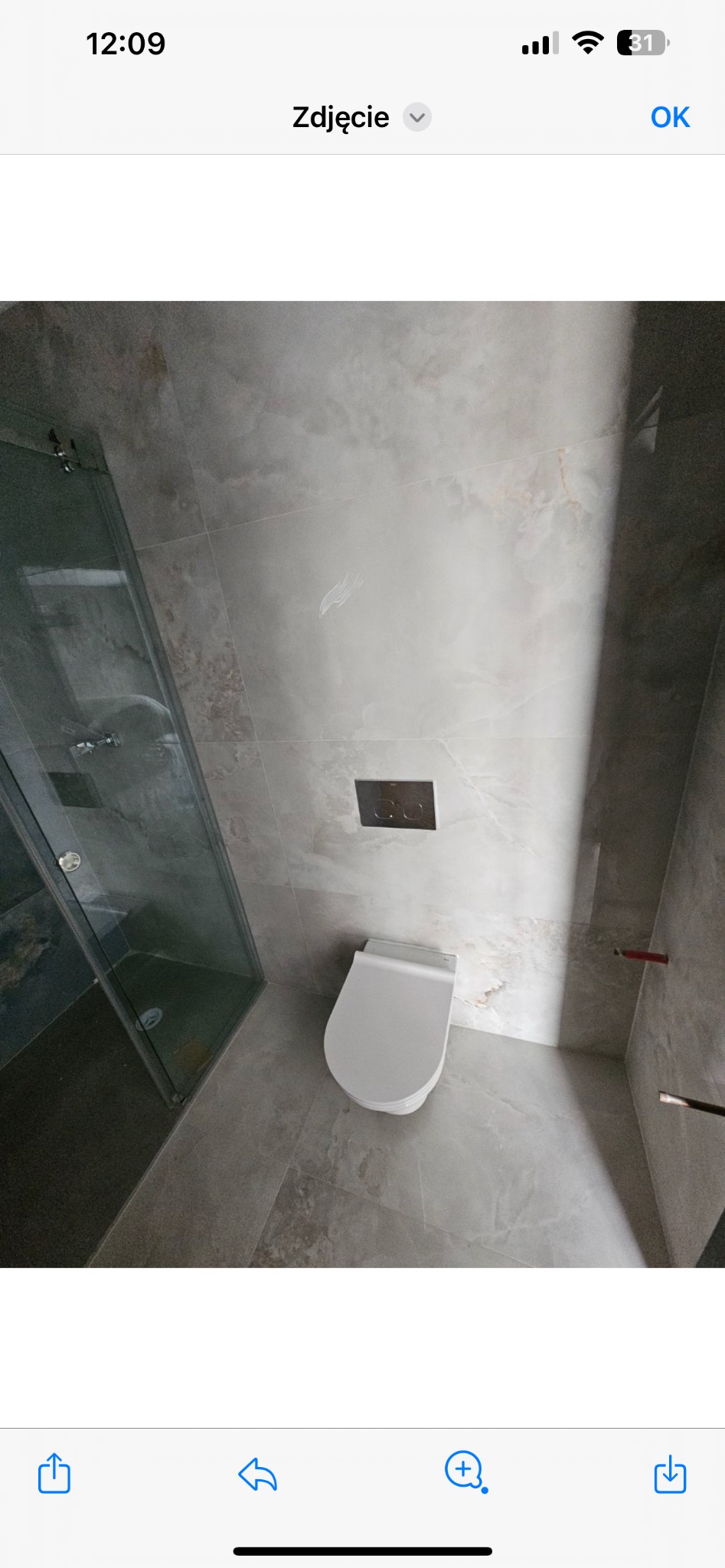 Nowoczesna łazienka z szarą marmurową okładziną, wisząca toaleta i szklana kabina prysznicowa, widok z góry.