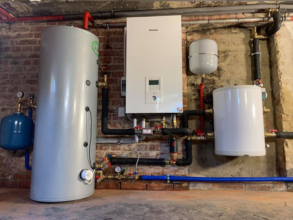 Instalacja grzewcza z kotłem Panasonic, zasobnikiem ciepłej wody i naczyniami przeponowymi na tle ściany z cegły