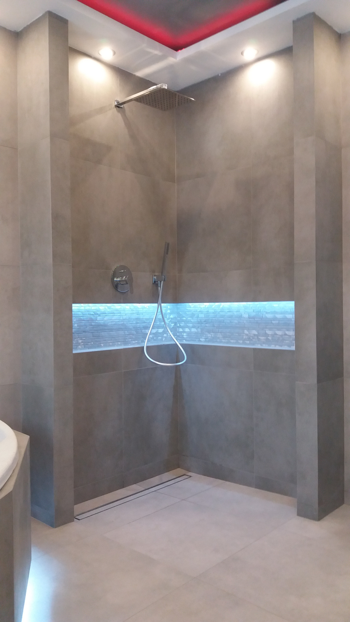 Nowoczesna kabina prysznicowa walk-in z szarymi płytkami, podświetlaną wnęką i odpływem liniowym w podłodze.