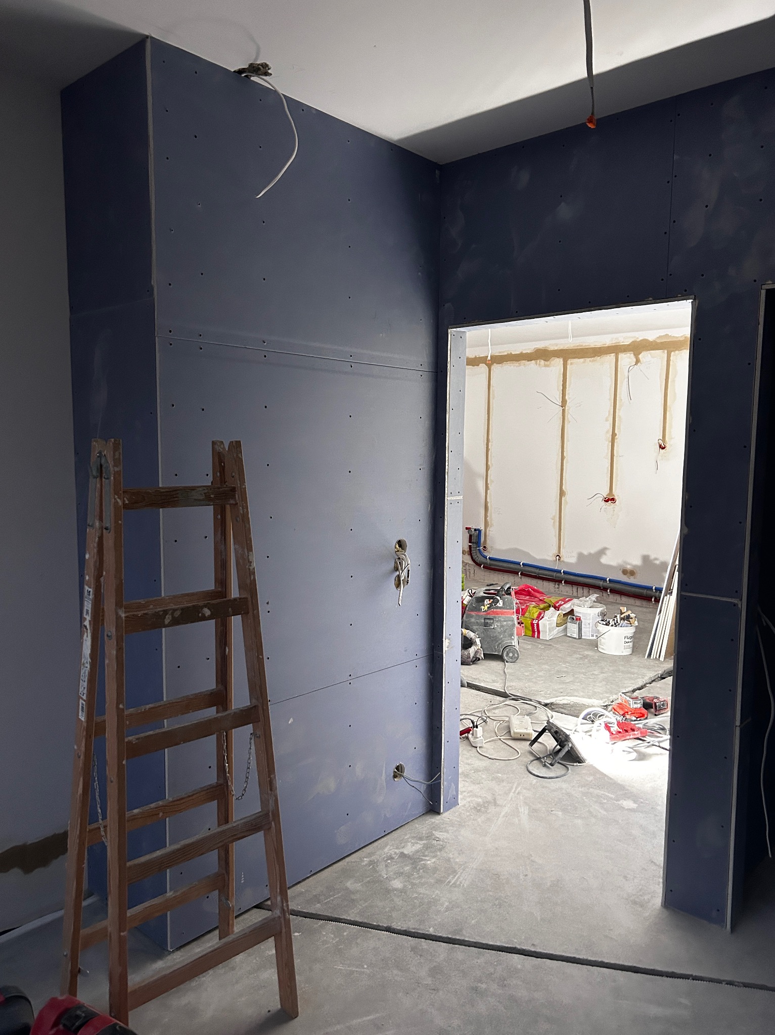 Montaż płyt karton-gips na ścianach w trakcie remontu. Widoczna drewniana drabina i przygotowane instalacje w tle, stan surowy.