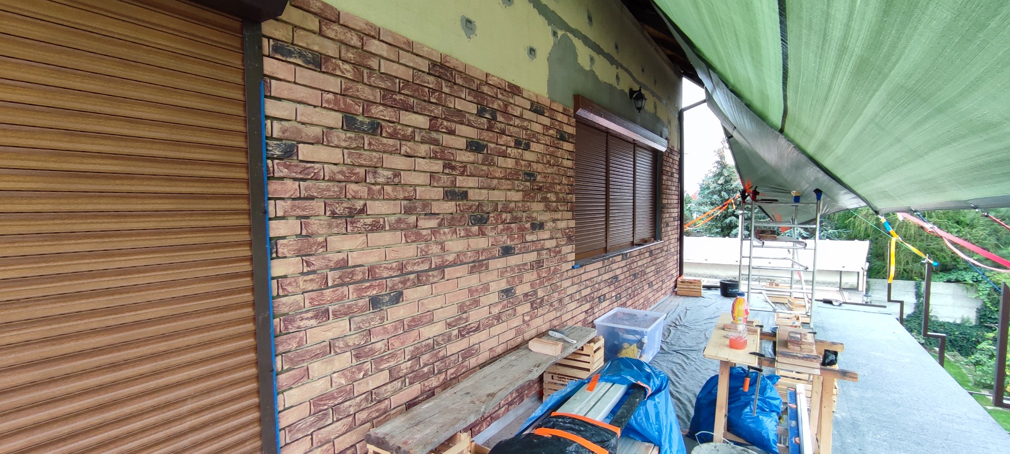 Klinkierowa okładzina ściany zewnętrznej budynku w trakcie montażu, widoczne elementy rusztowania i narzędzia pracy.