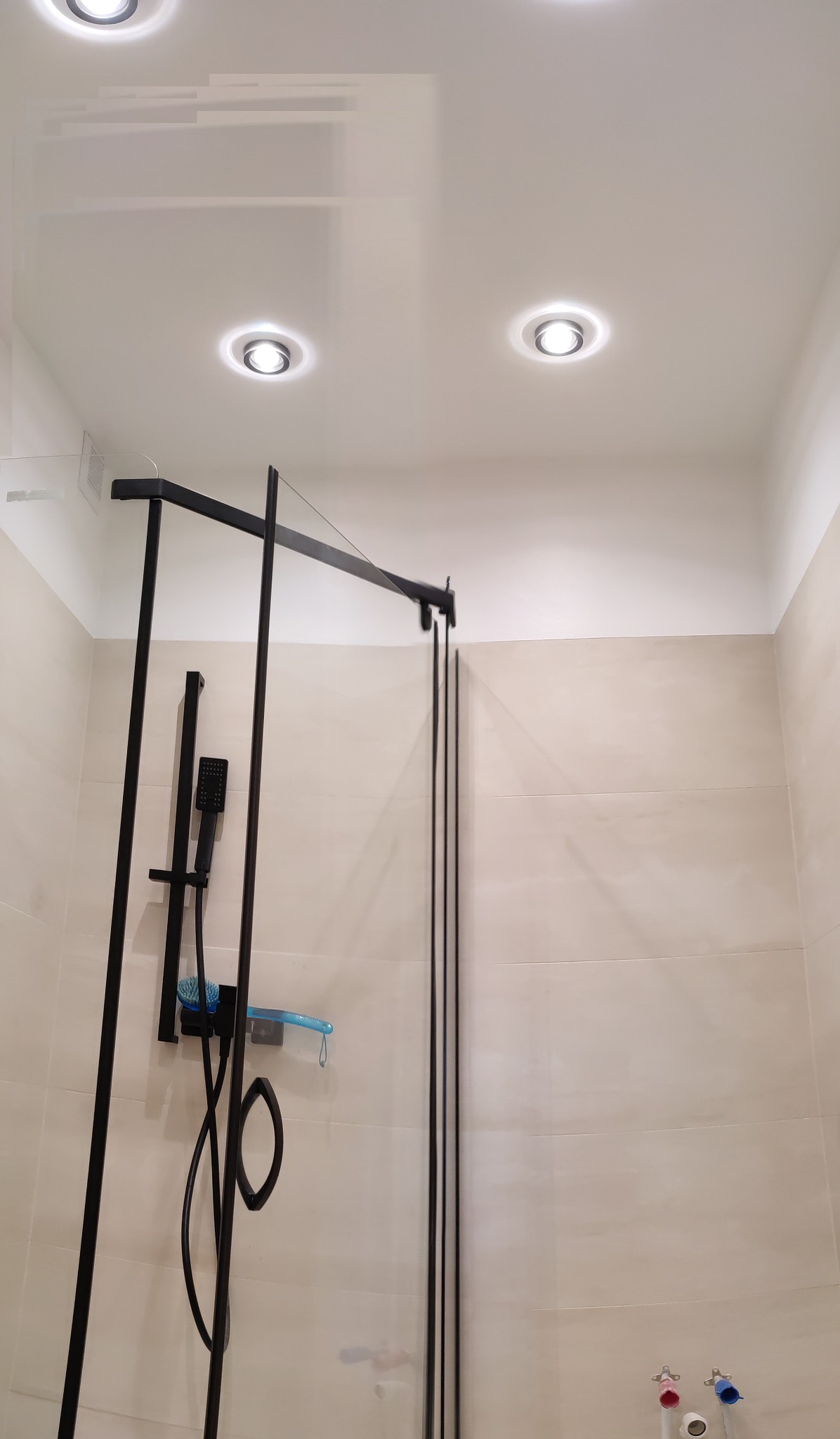 Nowoczesna kabina prysznicowa z czarnymi profilami i deszczownicą w łazience wykończonej beżowymi płytkami, oświetlenie punktowe w suficie.