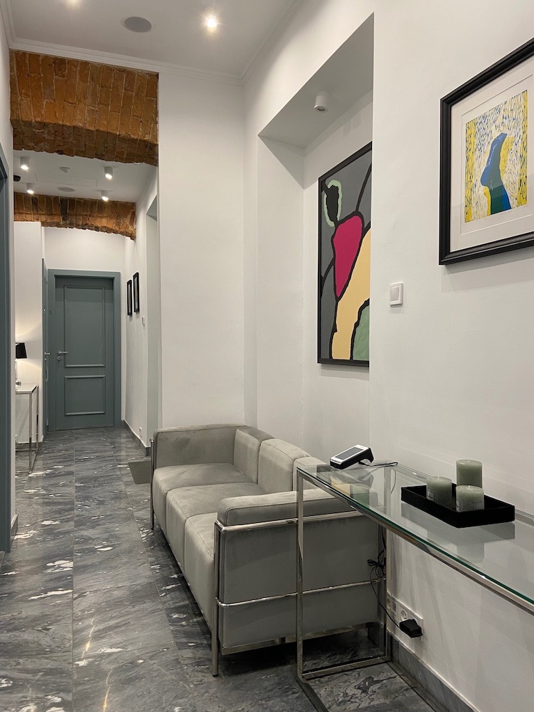 Wnętrze gabinetu z szarą sofą, szklanym stolikiem z trzema świecami, marmurową podłogą i ceglanym łukiem w suficie.