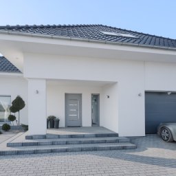 RG SYSTEM - Nowoczesny, biały dom jednorodzinny z szarą stolarką okienną i drzwiową, oraz z garażem z bramą segmentową, widok z zewnątrz.