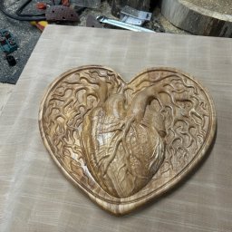 BAYWOOD - Ręcznie rzeźbiona drewniana płaskorzeźba w kształcie serca z motywem anatomicznego serca i korzeni drzewa, leżąca na drewnianym blacie w warsztacie.