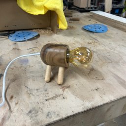 BAYWOOD - Drewniana lampka nocna w kształcie zwierzątka z żarówką Edison na warsztacie w Katowicach, w tle narzędzia i materiały stolarskie.