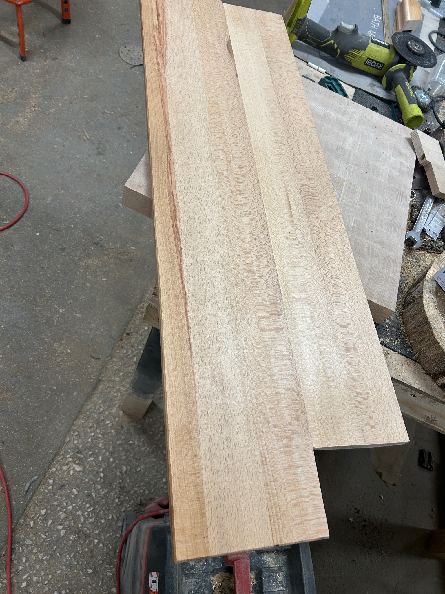 Surowy, jasny blat z drewna klonowego z wyraźnym rysunkiem słojów, leżący w warsztacie obok narzędzi i innych elementów drewnianych.