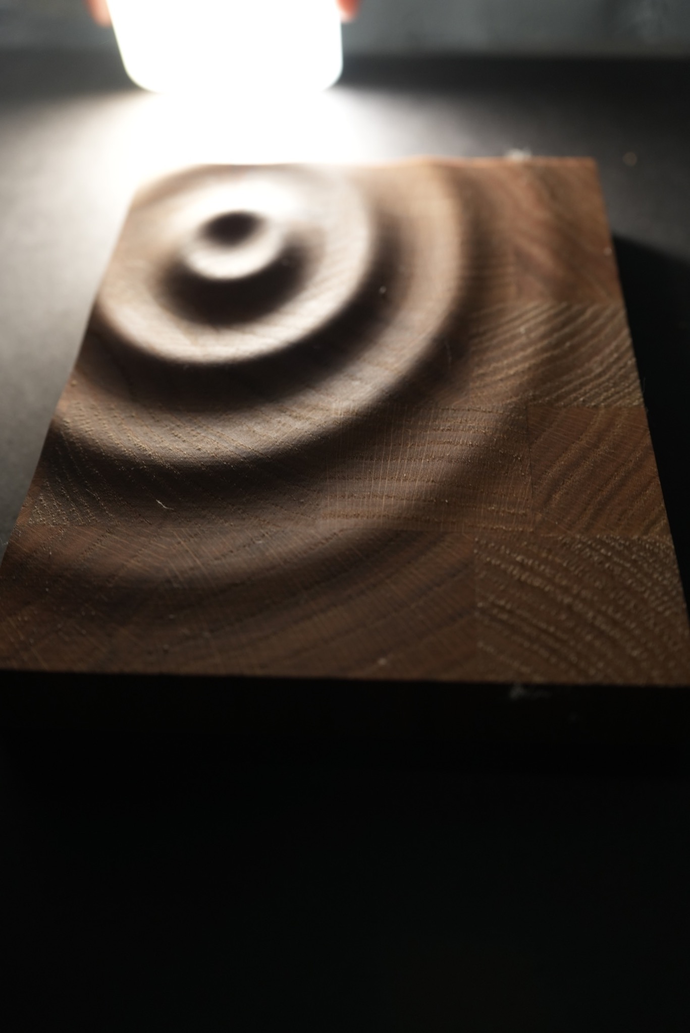 Drewniany blat z wyfrezowanymi koncentrycznymi okręgami, oświetlony od góry, ukazujący strukturę drewna.