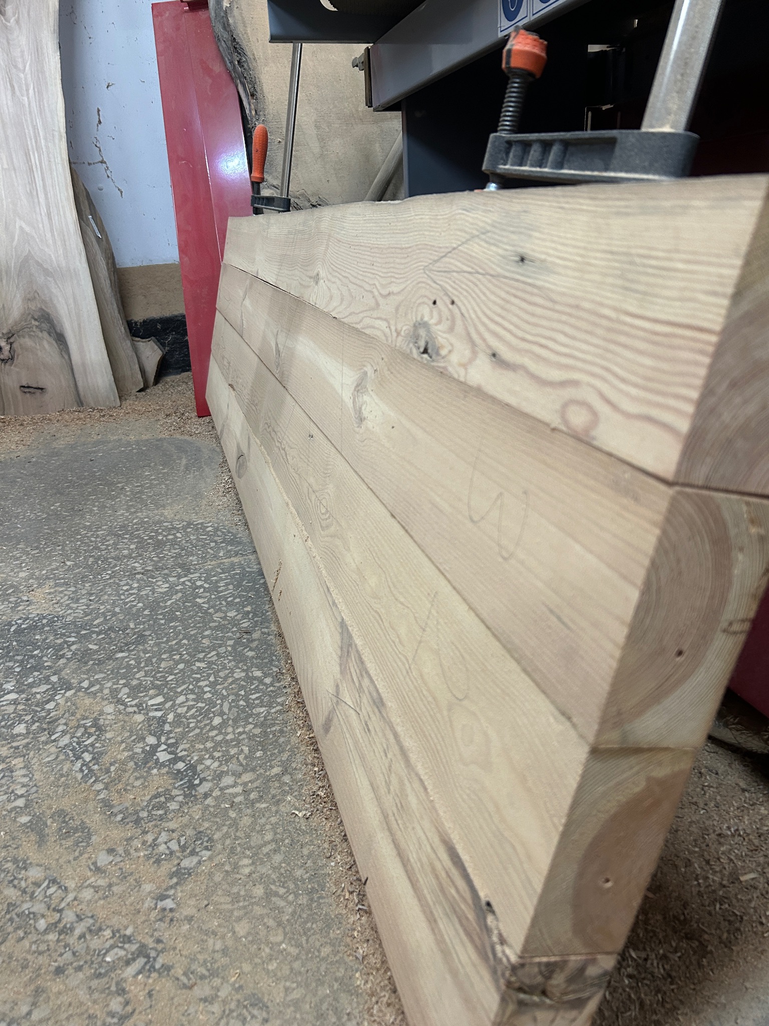 Przygotowany do obróbki drewniany element konstrukcyjny z widocznymi śladami ołówka i zamocowany ściskiem stolarskim, leżący w warsztacie.