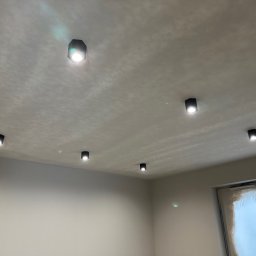 INSTAL ELEKT Volodymyr Dubovyk - Nowoczesne, czarne reflektory sufitowe LED równomiernie rozmieszczone w jasnym pomieszczeniu z oknem, minimalizm w oświetleniu wnętrza.