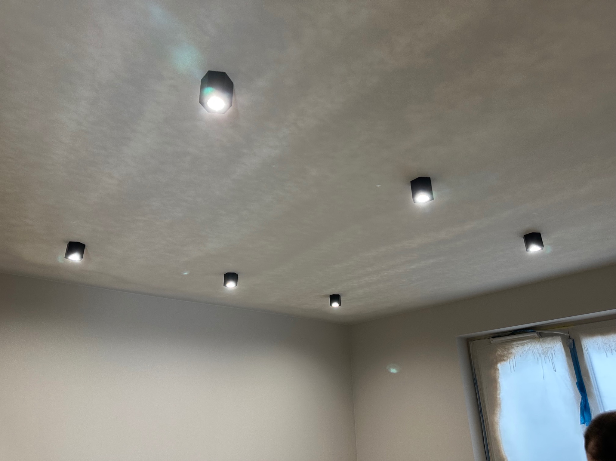 Nowoczesne, czarne reflektory sufitowe LED równomiernie rozmieszczone w jasnym pomieszczeniu z oknem, minimalizm w oświetleniu wnętrza.