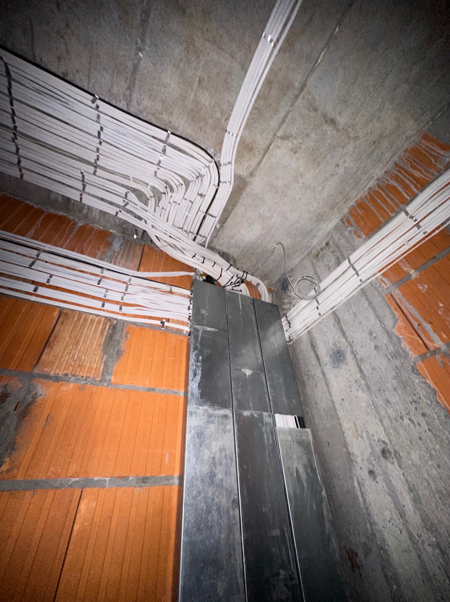 Rozprowadzenie kabli elektrycznych w peszlach na suficie w trakcie remontu w Warszawie. Widoczne kable, ściany z cegły i metalowa listwa.