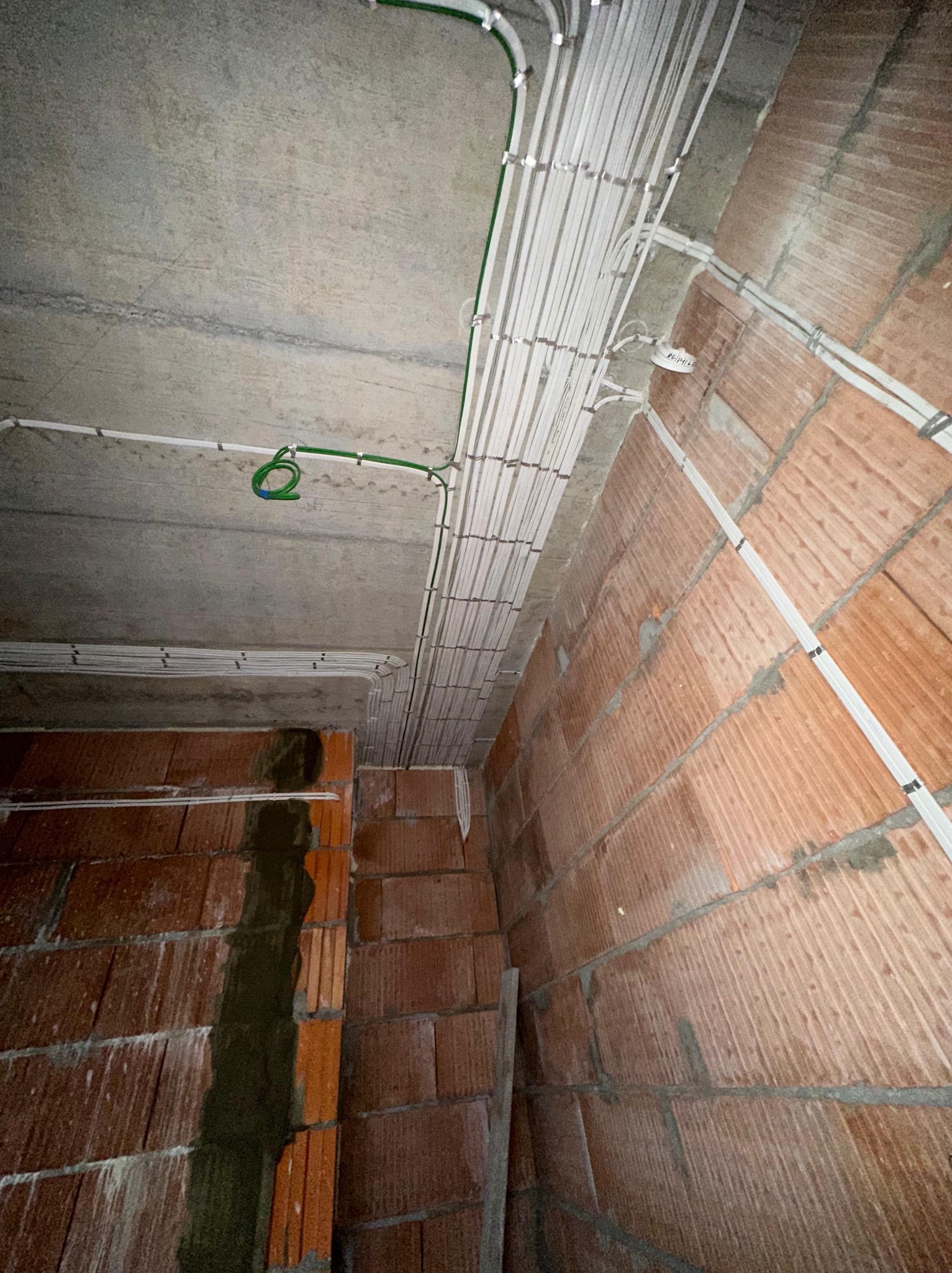 Rozprowadzenie przewodów elektrycznych w białych listwach na surowym suficie i ścianach z cegły. Widoczne kable w peszlach i puszki instalacyjne.