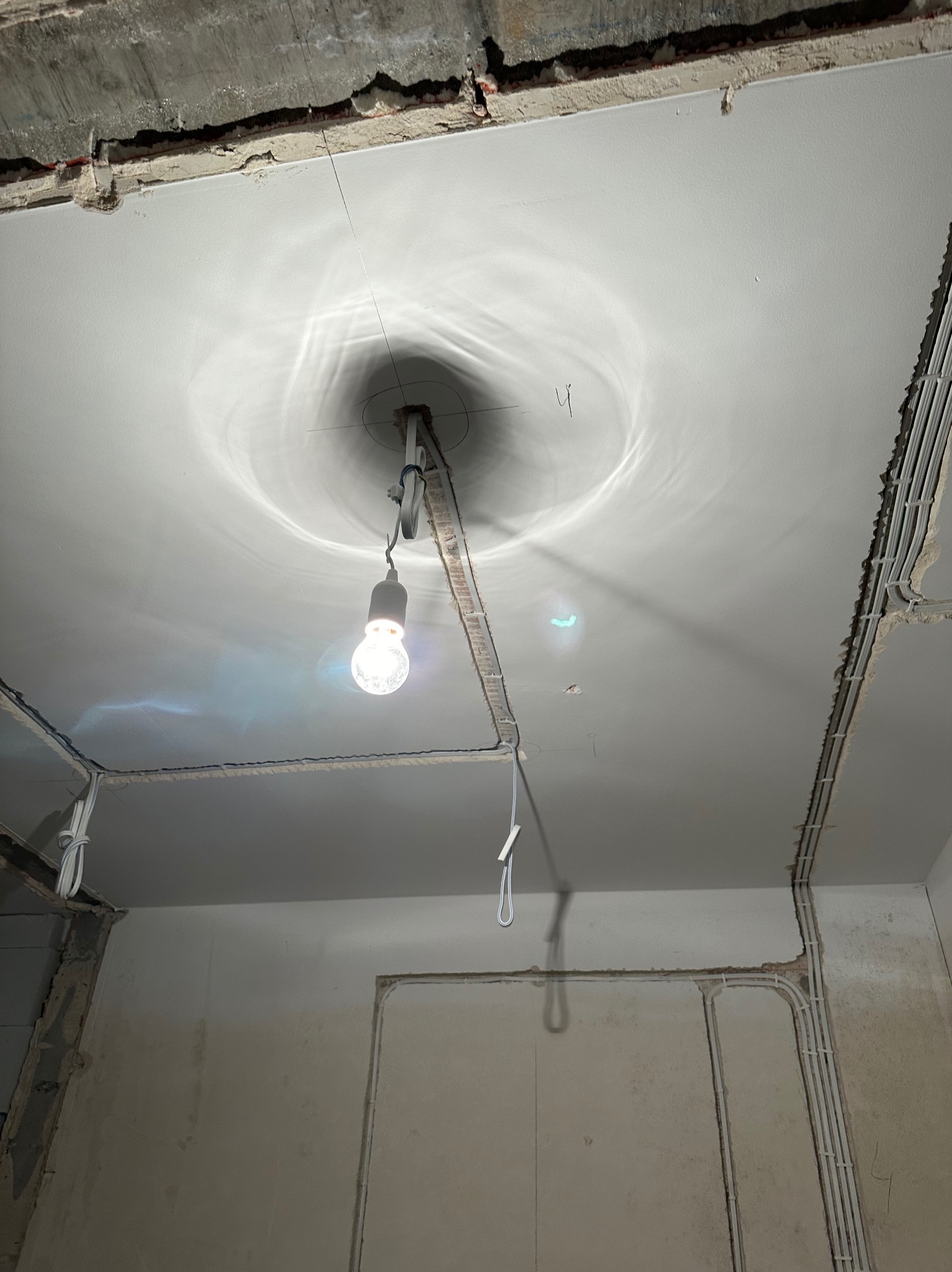 Montaż instalacji elektrycznej na suficie podwieszanym w trakcie remontu. Widoczne kable w korytach i żarówka tymczasowa.