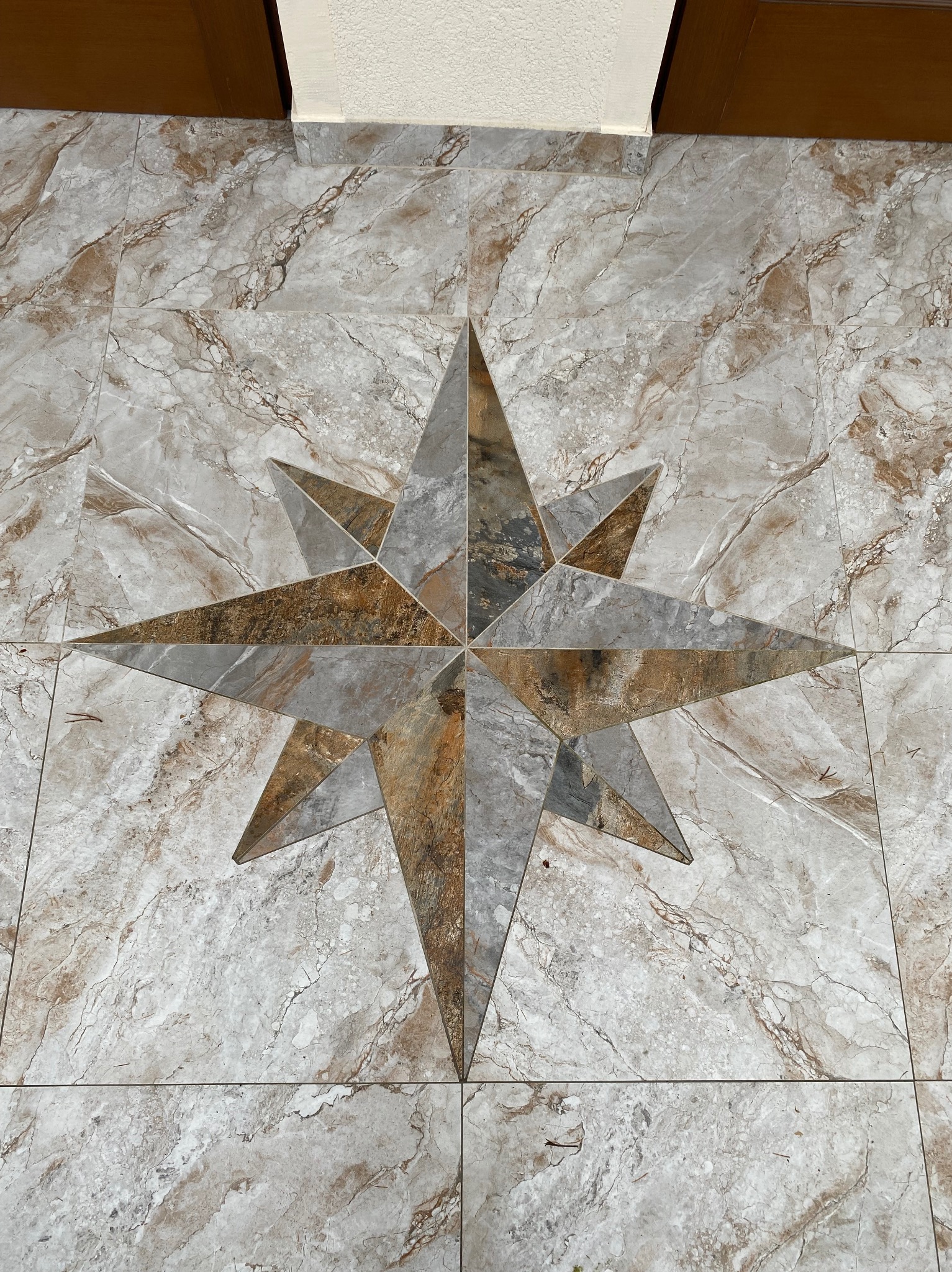 Wzorzysta podłoga z płytek imitujących marmur, z centralnie umieszczoną dekoracją w kształcie gwiazdy, wykonaną z płytek w odcieniach szarości i brązu. Widok z góry.
