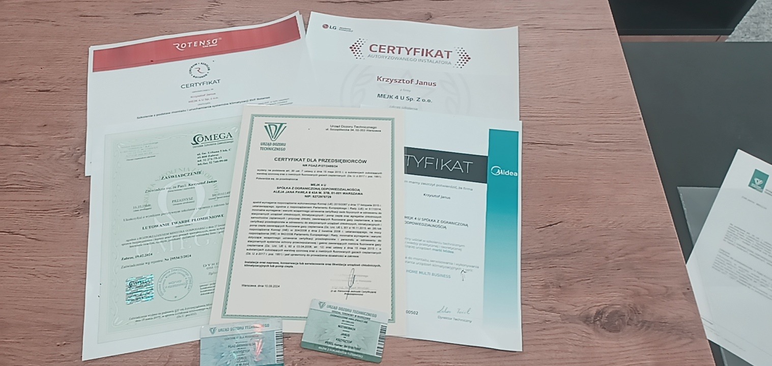 Zestaw certyfikatów i uprawnień instalatora z nazwami firm Rotenso, LG, Omega, Midea, Urząd Dozoru Technicznego, ułożonych na drewnianym blacie.
