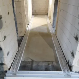 Przygotowanie podłoża pod podłogę w surowym wnętrzu z białych bloczków, widoczne metalowe profile pod instalacje.