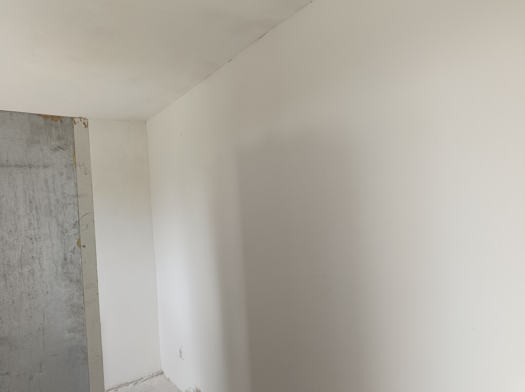 Świeżo pomalowane na biało ściany w rogu pokoju, z widocznym surowym wejściem do innego pomieszczenia z lewej strony, ukazujące etap prac wykończeniowych.