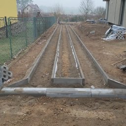 Len-Bud - Przygotowanie podłoża pod ścieżkę w ogrodzie: ułożone obrzeża betonowe z wysypanym żwirem w środkowej części, widok na posesje sąsiadów w tle.