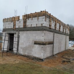 Len-Bud - Surowy stan budynku z bloczków betonowych w trakcie budowy, z widocznym szalunkiem na stropie i wystającymi prętami zbrojeniowymi, na tle pochmurnego nieba.