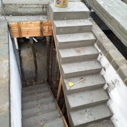 Len-Bud - Surowe betonowe schody w trakcie budowy w Smogórach, widoczne drewniane szalunki i wiadro z zaprawą, żółta miara leży na jednym ze stopni.