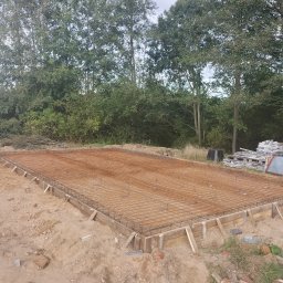 Len-Bud - Przygotowanie zbrojenia i szalunku pod płytę fundamentową na gruncie piaszczystym, widoczne drzewa w tle.