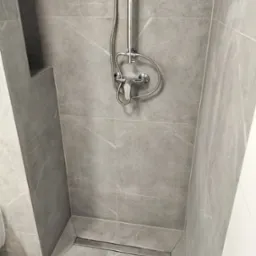 Wykończony prysznic w Smogóry z szarymi płytkami imitującymi marmur i odpływem liniowym, widok z góry na zamontowaną baterię.