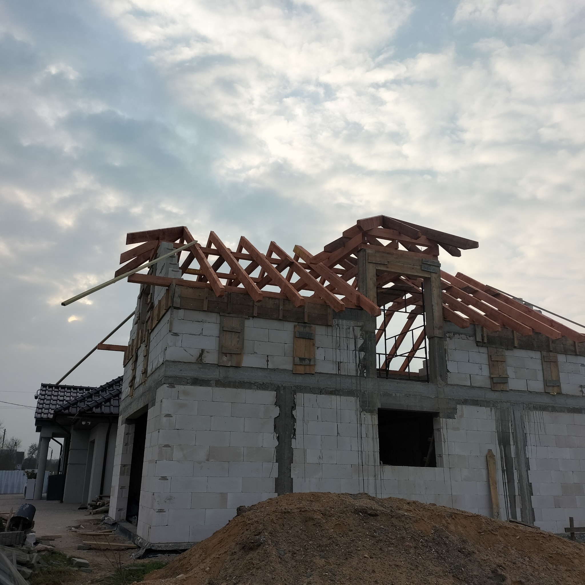 Surowy stan budynku z białego bloczka z drewnianą konstrukcją dachu w trakcie budowy, widoczne szare niebo