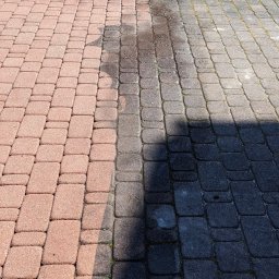 SOLID WORK Grzegorz Nieleszczuk - Częściowo umyta kostka brukowa: po lewej stronie różowa, czysta kostka, po prawej ciemna, brudna kostka, w środku mokry pas po myciu.