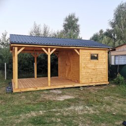 DANDREW SPÓŁKA Z OGRANICZONĄ ODPOWIEDZIALNOŚCIĄ - Drewniana altana z zadaszeniem z blachy trapezowej, widok z zewnątrz na trawniku. Elementy konstrukcyjne z surowego drewna, widoczne łączenia. Tło: zieleń drzew.