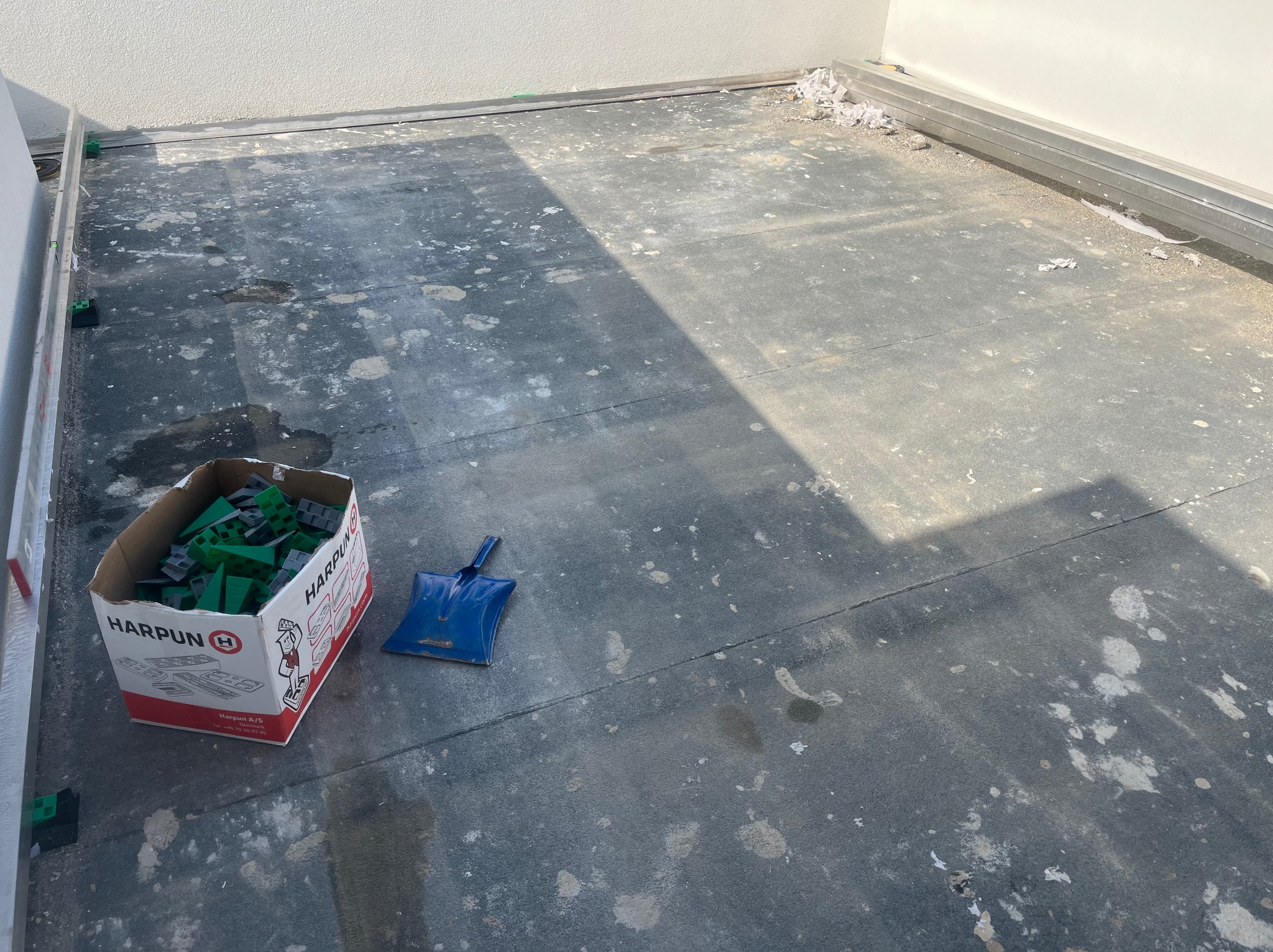 Przygotowanie podłoża pod taras: hydroizolacja, listwy obwodowe, pudełko z podkładkami dystansowymi i niebieska szpachelka na czarnej membranie.