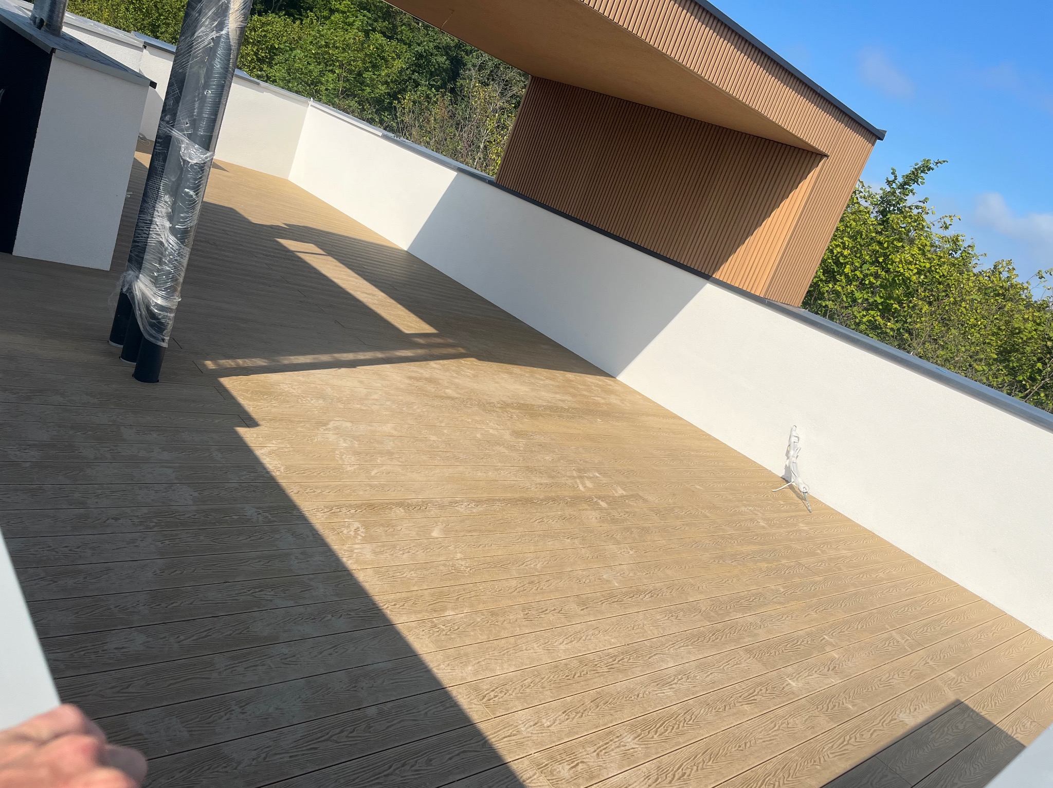 Jasny taras kompozytowy z białymi ścianami i elementami z drewna, w słoneczny dzień. Widok z góry na deski z wyraźnym wzorem drewna i cień.