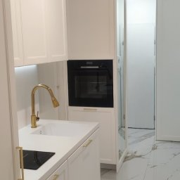 MR-STYL MEBLE NA WYMIAR - Biała zabudowa kuchenna z piekarnikiem, złotą armaturą i płytą indukcyjną, marmurowe płytki podłogowe.