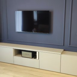 MR-STYL MEBLE NA WYMIAR - Nowoczesna zabudowa RTV z szarymi frontami, na tle ściany w kolorze granatowym z dekoracyjnymi listwami, widoczny głośnik Marshall i oczyszczacz powietrza Dyson.