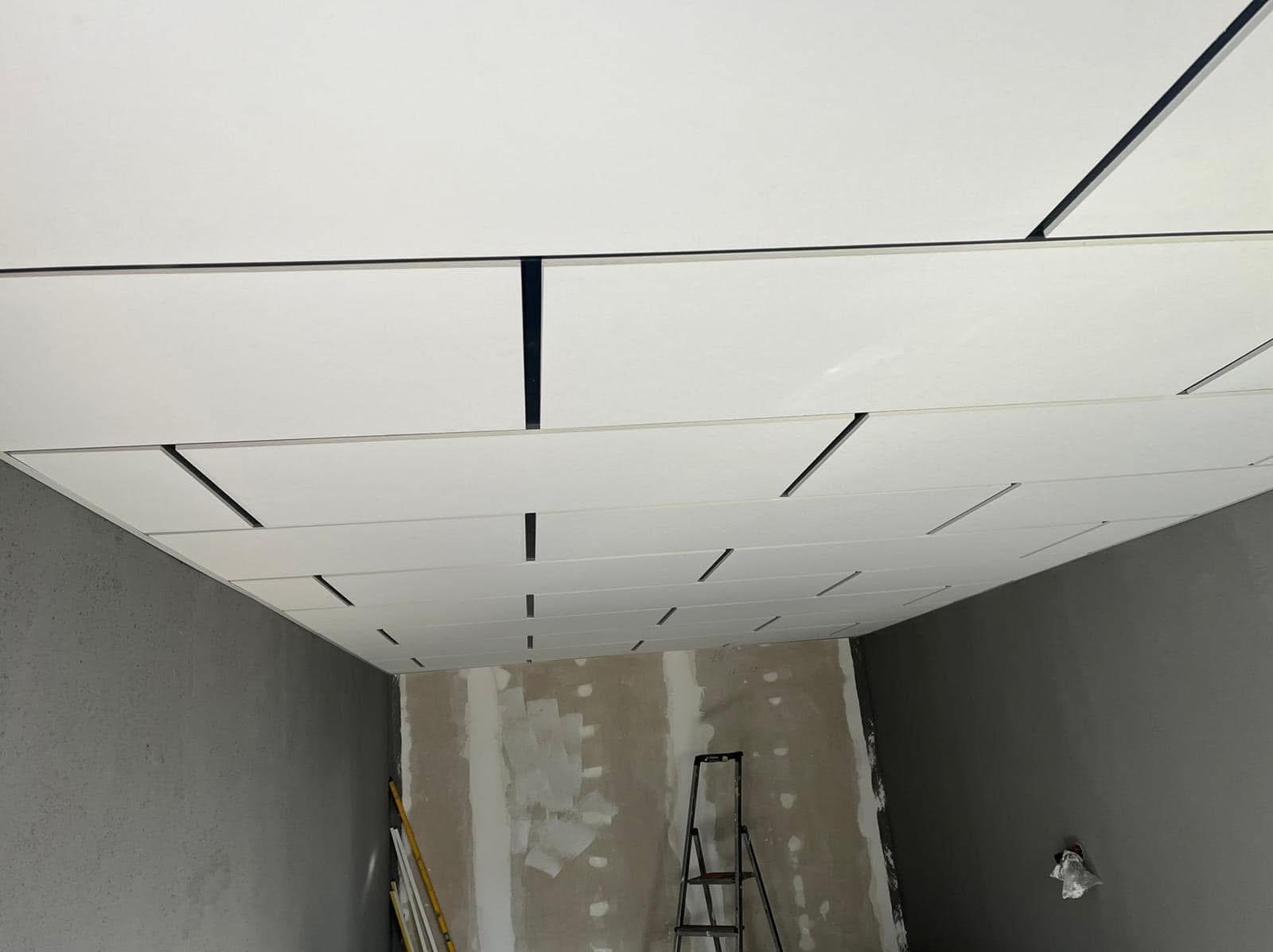 Montaż sufitu podwieszanego z widocznymi elementami konstrukcyjnymi, drabina w tle, ściany w stanie surowym.