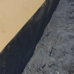 Fundament domu w trakcie budowy, zabezpieczony folią kubełkową i zasypany piaskiem.