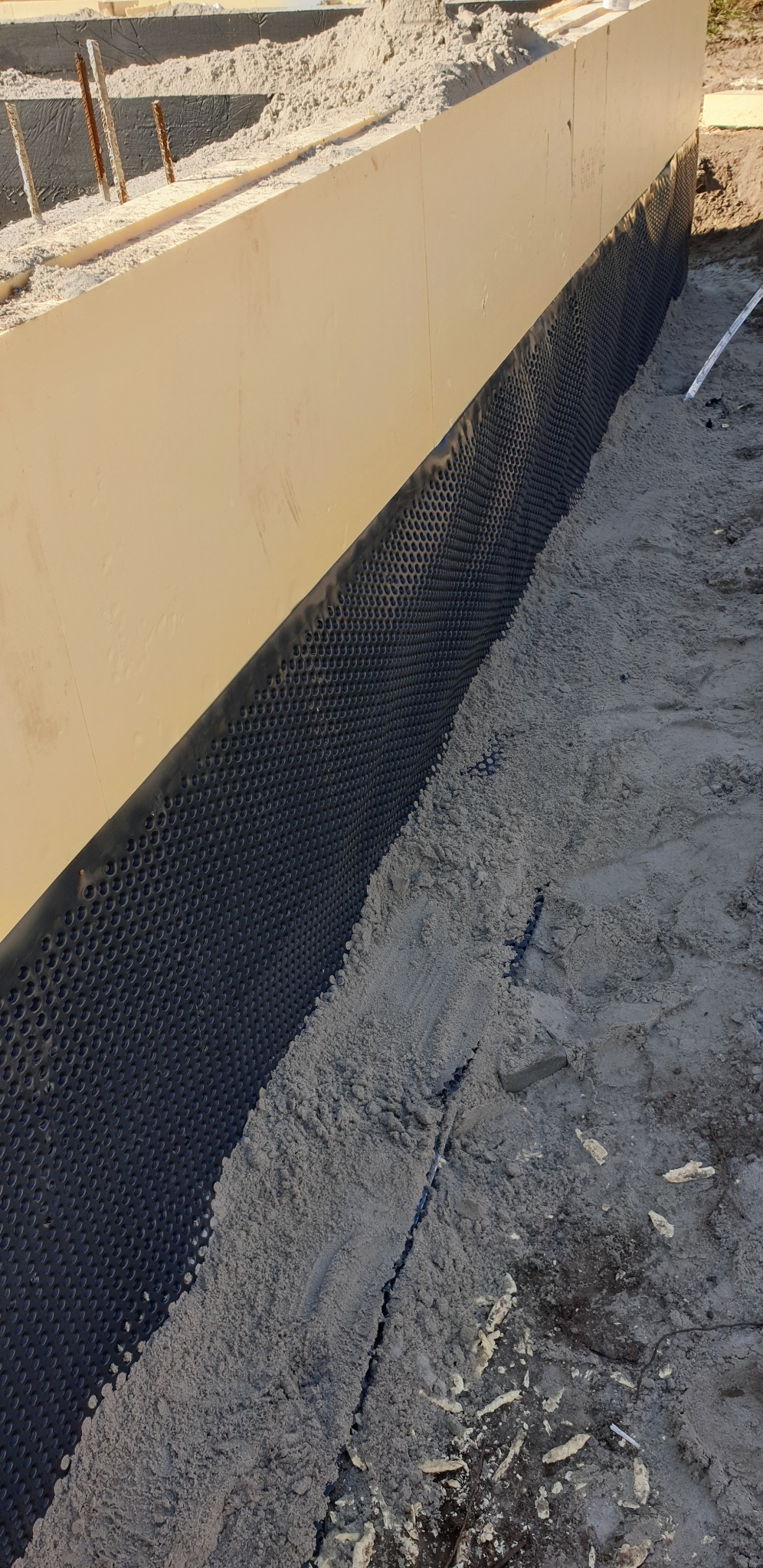 Fundament domu w trakcie budowy, zabezpieczony folią kubełkową i zasypany piaskiem.