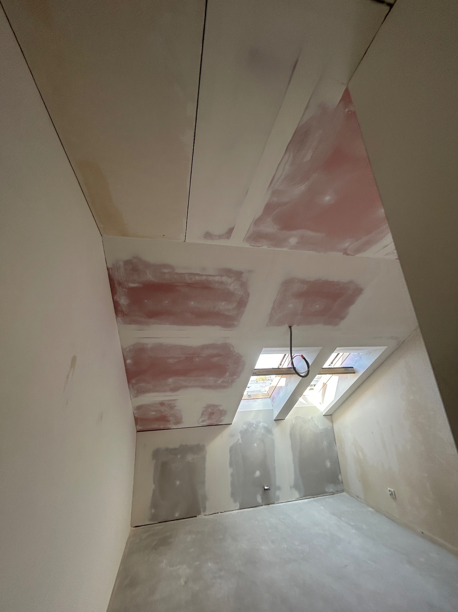 Poddasze w trakcie prac wykończeniowych: sufit z płyt kartonowo-gipsowych z widocznymi łączeniami, ściany częściowo pokryte gładzią, okna dachowe.