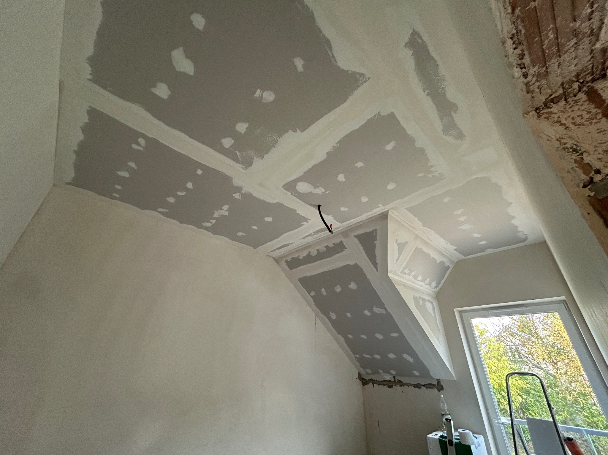 Poddasze po montażu płyt gipsowo-kartonowych na skośnym suficie, widoczne łączenia płyt i szpachlowane miejsca wkrętów. Częściowo widoczna ściana z cegły.