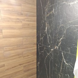 Robert Ziółkowski Usługi Ogólnobudowlane - Ściana wyłożona dwoma rodzajami płytek: imitacją drewna w odcieniach brązu oraz czarnymi płytkami z białym marmurkowym wzorem, widoczne łączenia między płytkami.